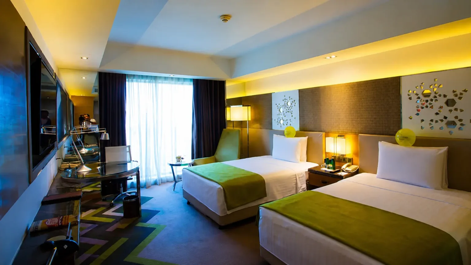 A modern hotel guest room with two twin beds, lime green accents, a work desk, and ambient lighting at Courtyard by Marriott Agra.