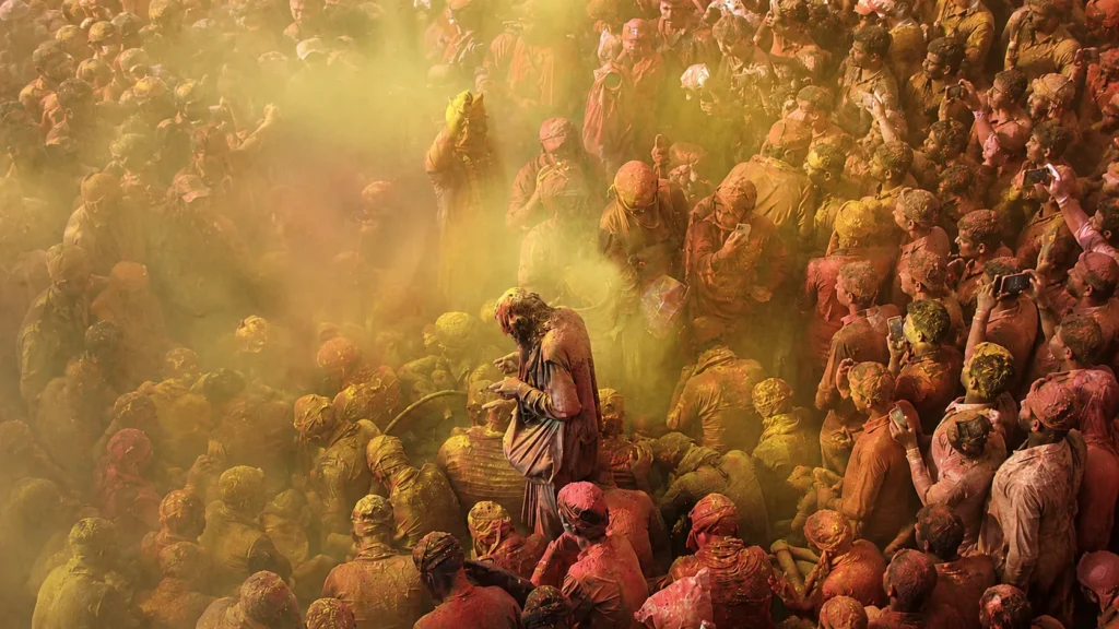 Devotees immersed in vibrant yellow and red Holi colors during a traditional celebration in Vrindavan, India, captured from above amidst a lively crowd.