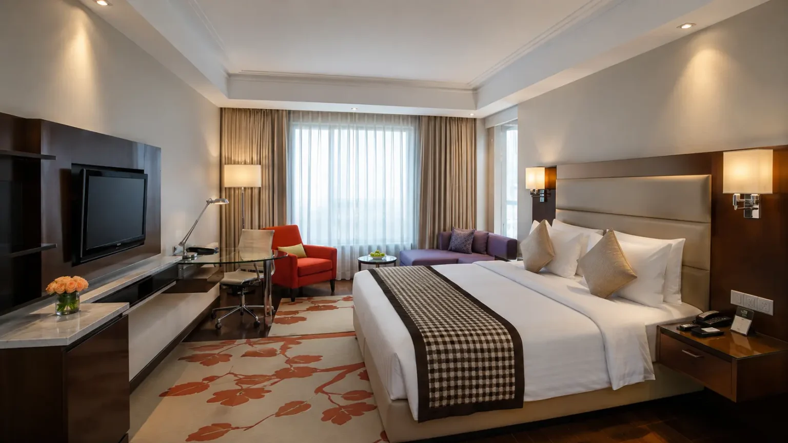 A spacious premium hotel room with a king-size bed, patterned rug, orange armchair, and large window at Holiday Inn Agra.