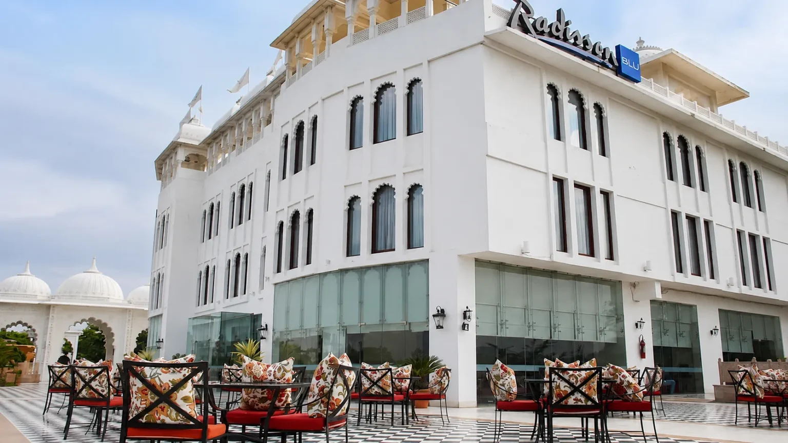 Exterior view of Radisson Blu Udaipur Palace Resort & Spa featuring elegant white Rajasthani-inspired architecture, spacious outdoor seating, and luxurious surroundings in Udaipur, Rajasthan.