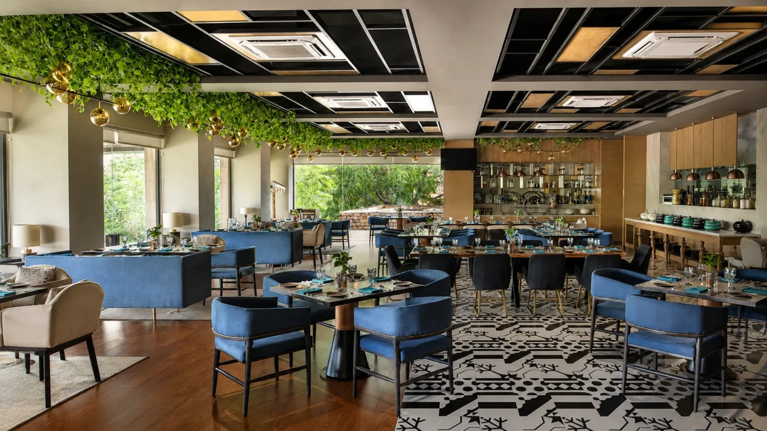 Modern all-day dining restaurant at Novotel Jodhpur ITI Circle featuring contemporary interiors, elegant blue seating, greenery, and a stylish ambience for breakfast, lunch, and dinner.