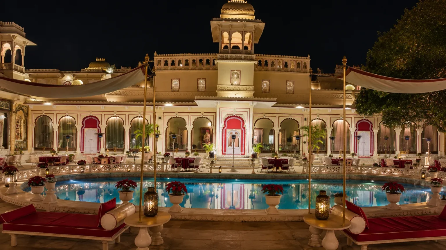 Illuminated façade of Shiv Niwas Palace Udaipur with a heritage courtyard, elegant pool, traditional arches, and royal architecture glowing under the evening sky.