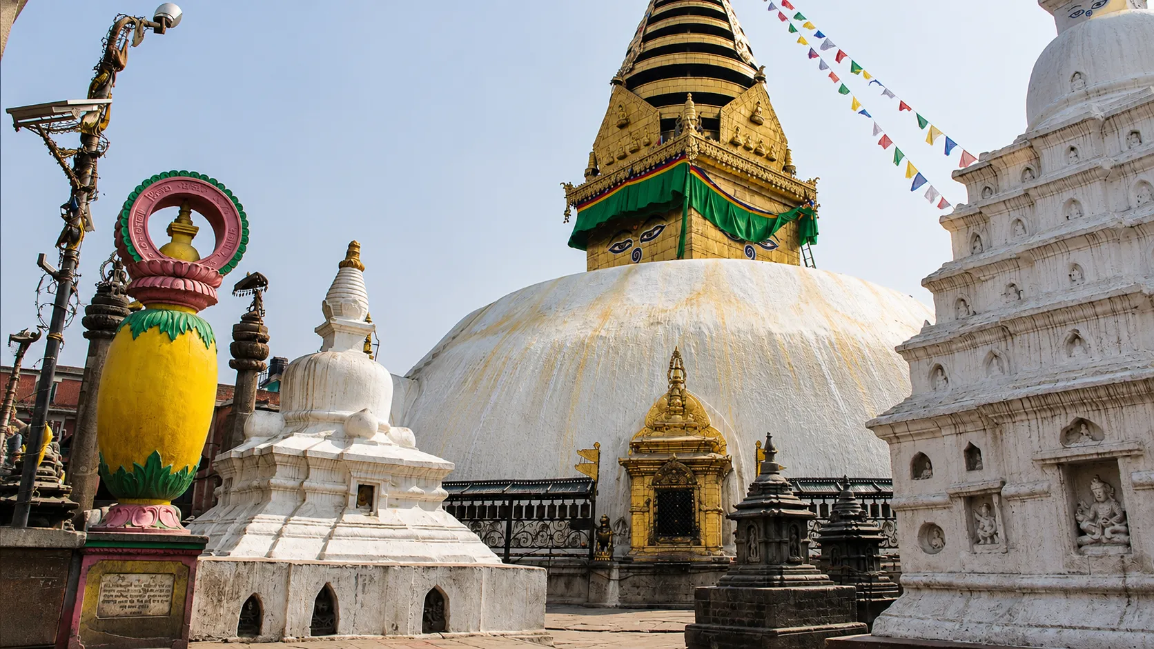 The historic Swayambhunath Stupa in Kathmandu, Nepal, featuring its white dome, golden spire, Buddha eyes, and colorful prayer flags.