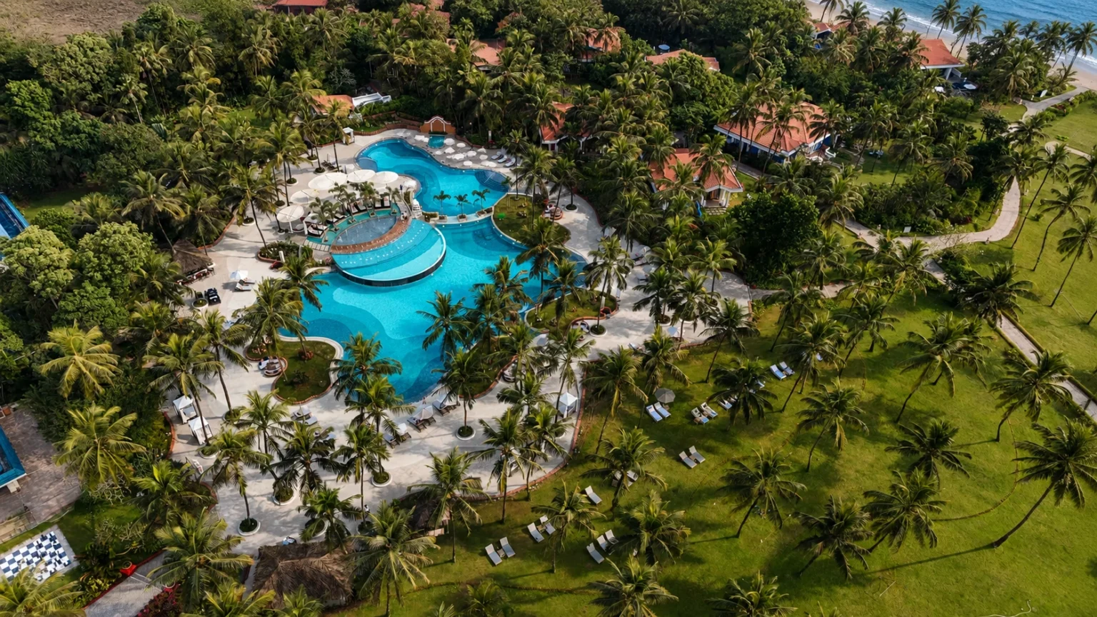Aerial view of Taj Exotica Resort & Spa Goa featuring expansive swimming pools, lush tropical gardens, and direct beachfront access.