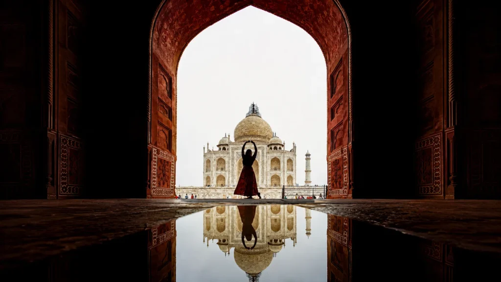 Top Places to Visit in Agra: Your Travel Guide 1 Silhouette of a visitor standing beneath a grand Mughal arch with the Taj Mahal perfectly reflected in a pool of water in Agra, India.