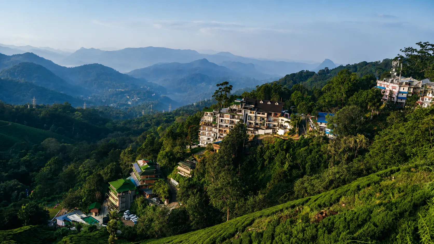 Panoramic view of Munnar's lush tea plantations, forested hills, and hillside resorts overlooking the mist-covered Western Ghats in Kerala, India.
