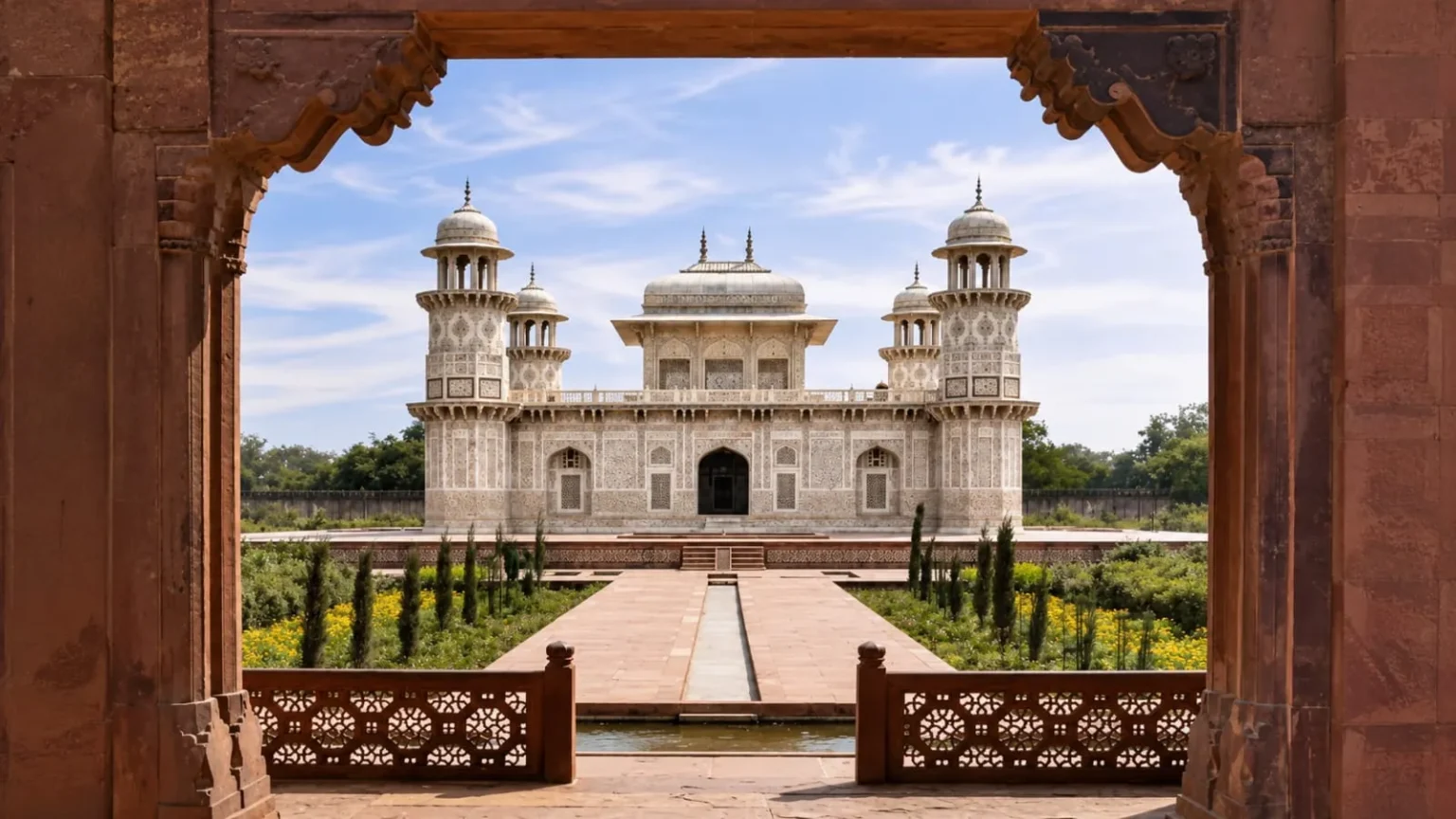 Elegant white marble tomb of Itmad-ud-Daulah framed by a Mughal sandstone archway in Agra, India.