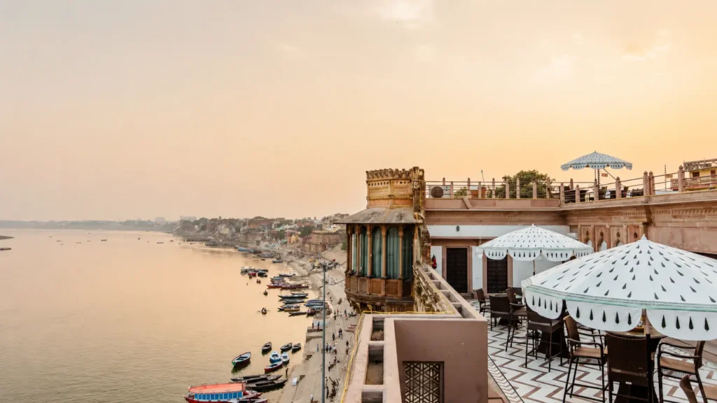 Luxury riverside hotel terrace overlooking the Ganges River and Varanasi ghats at sunrise with elegant outdoor seating.