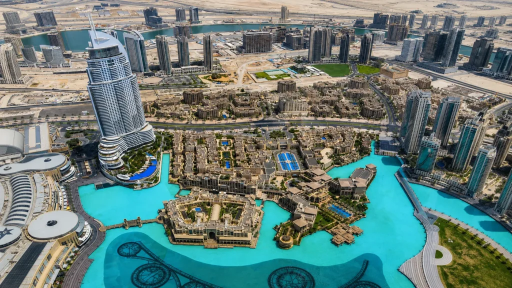 Panoramic aerial view of Downtown Dubai featuring luxury skyscrapers, turquoise Dubai Fountain Lake, and modern architecture under a clear daytime sky.