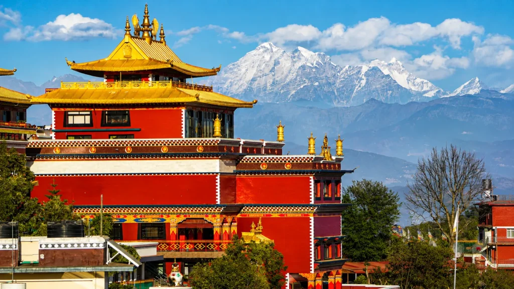 Red and gold Buddhist temple with snow-capped Himalayan mountains in the background under a clear blue sky