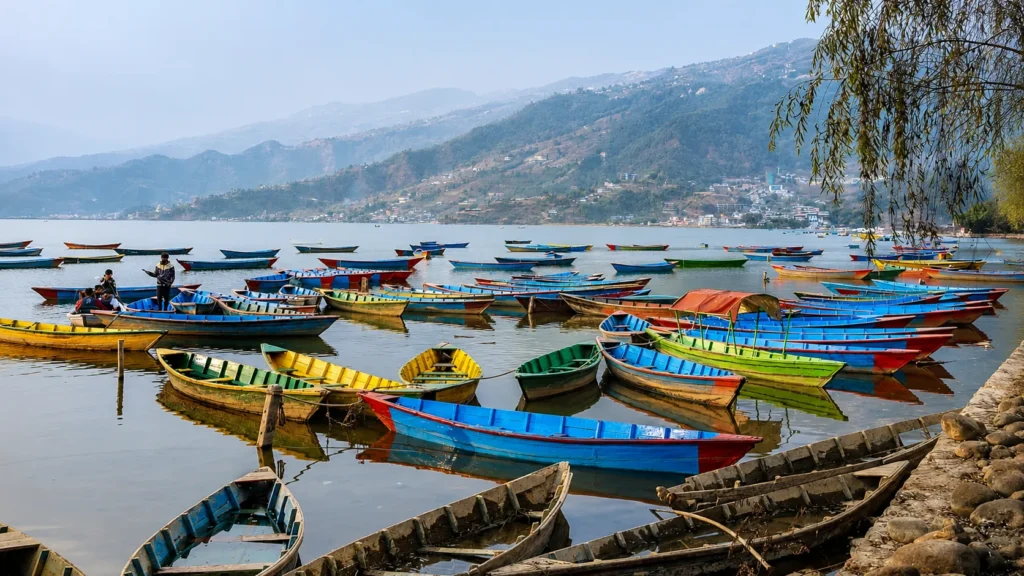 Colorful wooden boats floating on Phewa Lake with forested hills and mountain scenery in the background