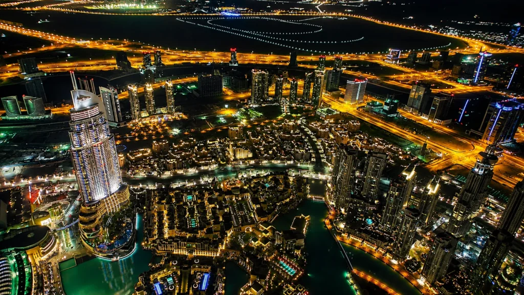Aerial night view of Downtown Dubai featuring illuminated skyscrapers, luxury towers, highways, and vibrant city lights from above.