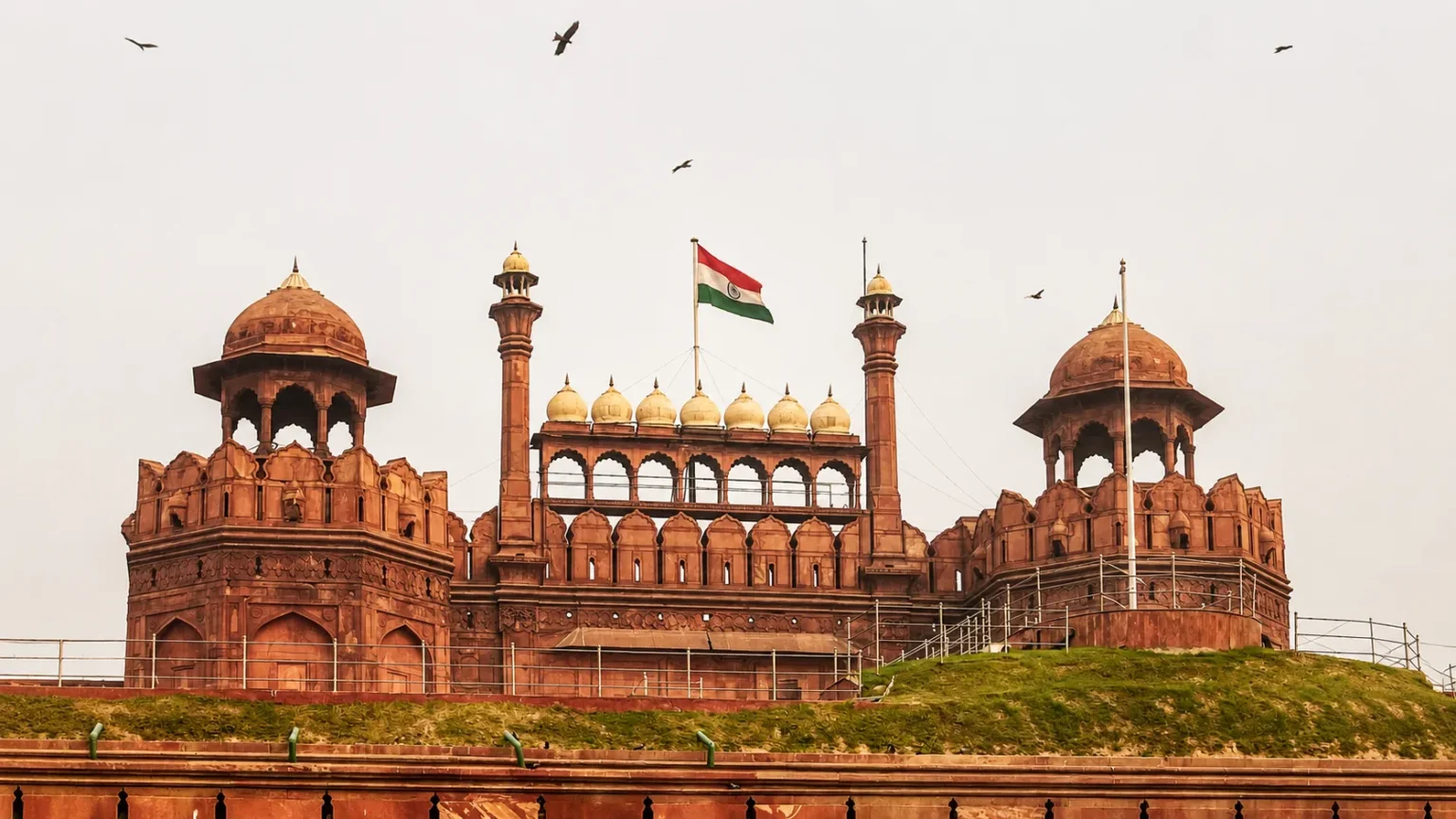 Historic Red Fort in Delhi with its red sandstone architecture, domed pavilions, minarets, and the Indian national flag flying above.