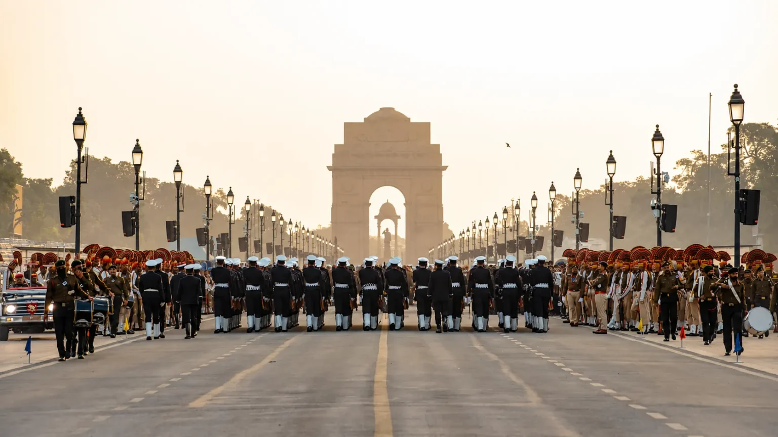 Republic Day parade with uniformed personnel marching along Kartavya Path toward India Gate, surrounded by ceremonial formations.