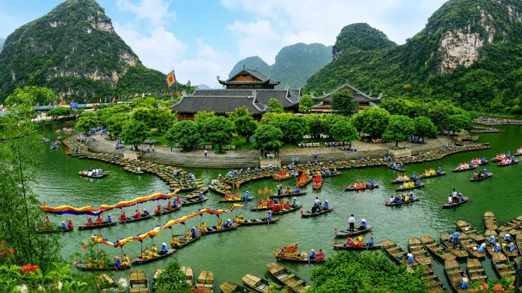 Traditional wooden boats carrying visitors through the emerald waterways of Trang An Scenic Landscape Complex, surrounded by limestone karst mountains and lush greenery in Ninh Binh, Vietnam.