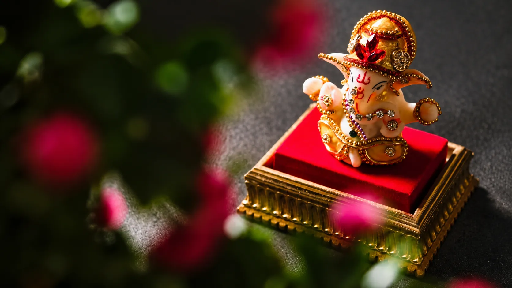 Decorated Lord Ganesha idol wearing a golden crown and jewelry on a red velvet pedestal