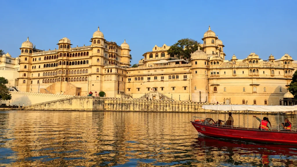 Historic City Palace of Udaipur overlooking Lake Pichola, with a red tourist boat cruising across the water