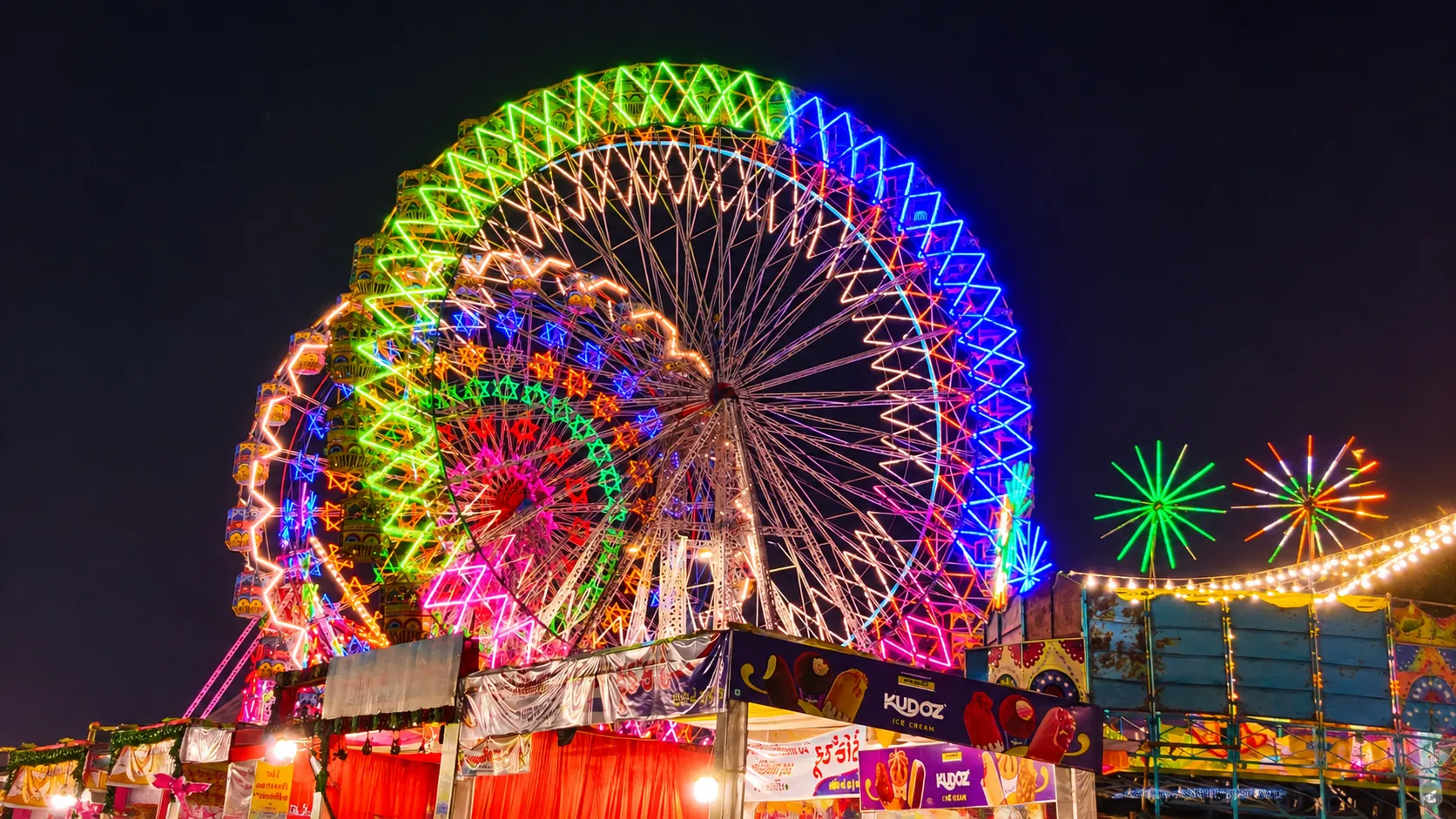 Large brightly illuminated Ferris wheel glowing with colorful lights at a festive Dussehra fair at night