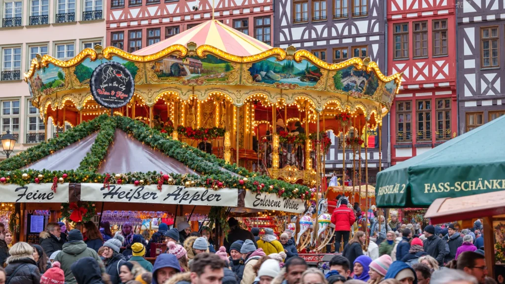 Festive German Christmas market with a brightly lit carousel, decorated stalls, and historic half-timbered buildings