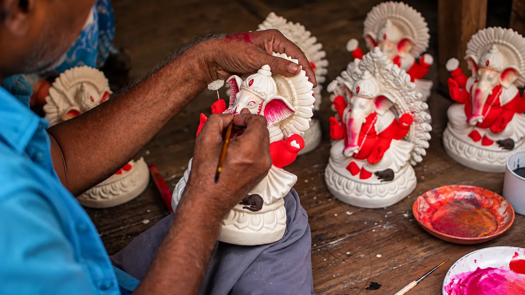 Indian artisan carefully painting red details on a white Ganesha idol in a traditional workshop