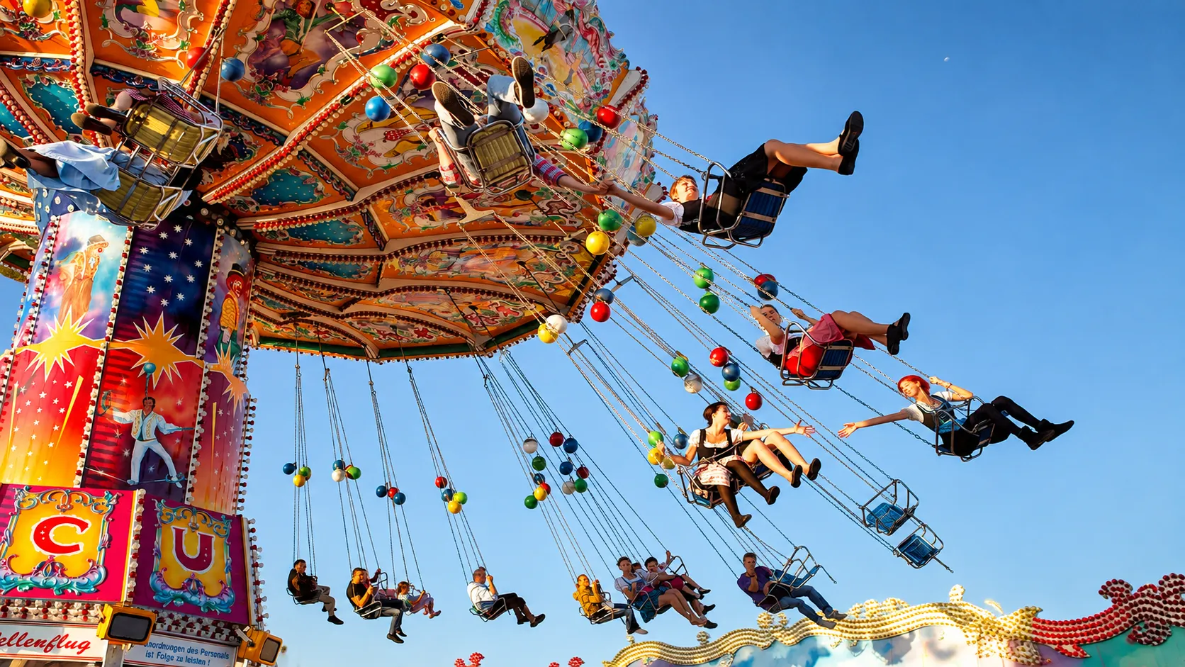 People enjoying a colorful chair swing ride at a German festival beneath a clear blue sky