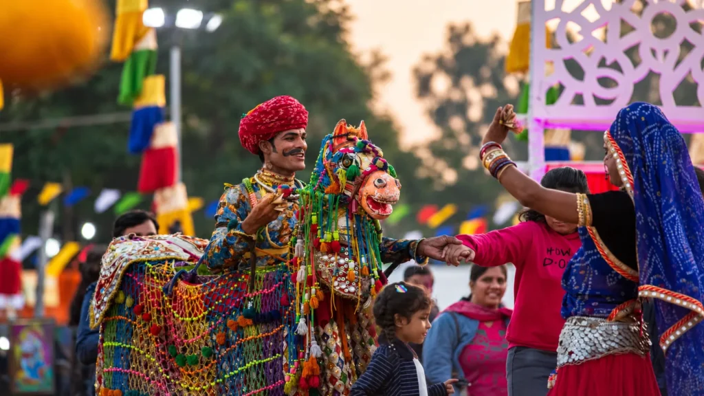 Rajasthani folk performer in colorful traditional attire performing with a decorated wooden horse puppet during a cultural celebration.