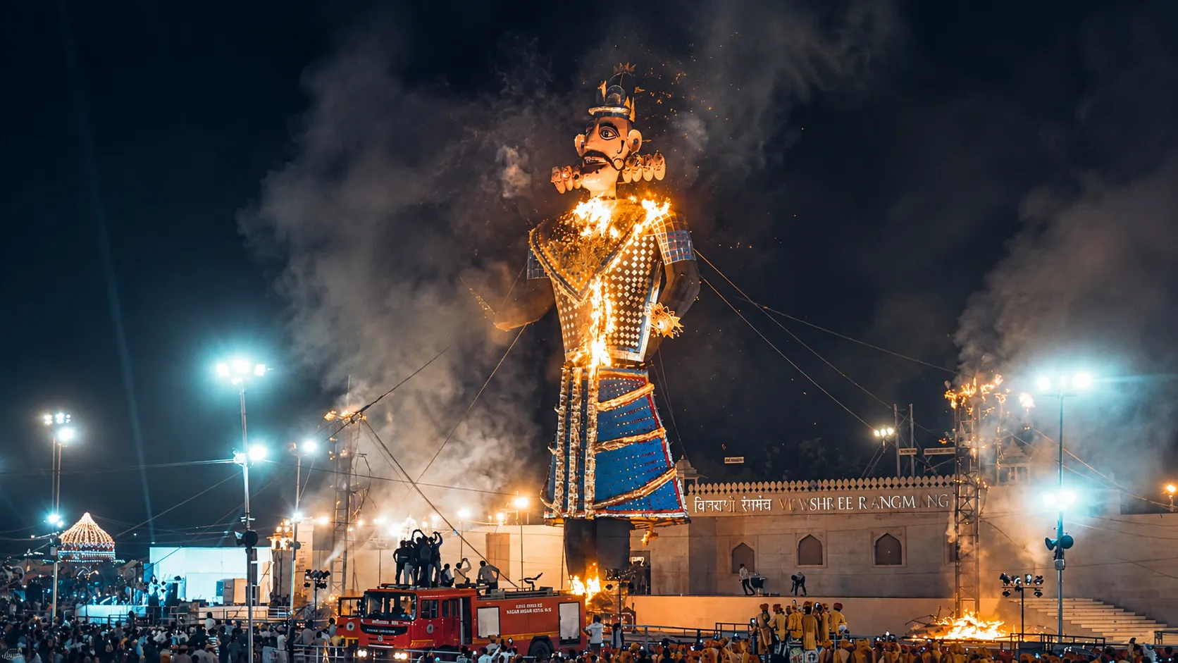 Giant Ravana effigy burning during a nighttime Dussehra celebration with crowds, fire, smoke, and illuminated grounds