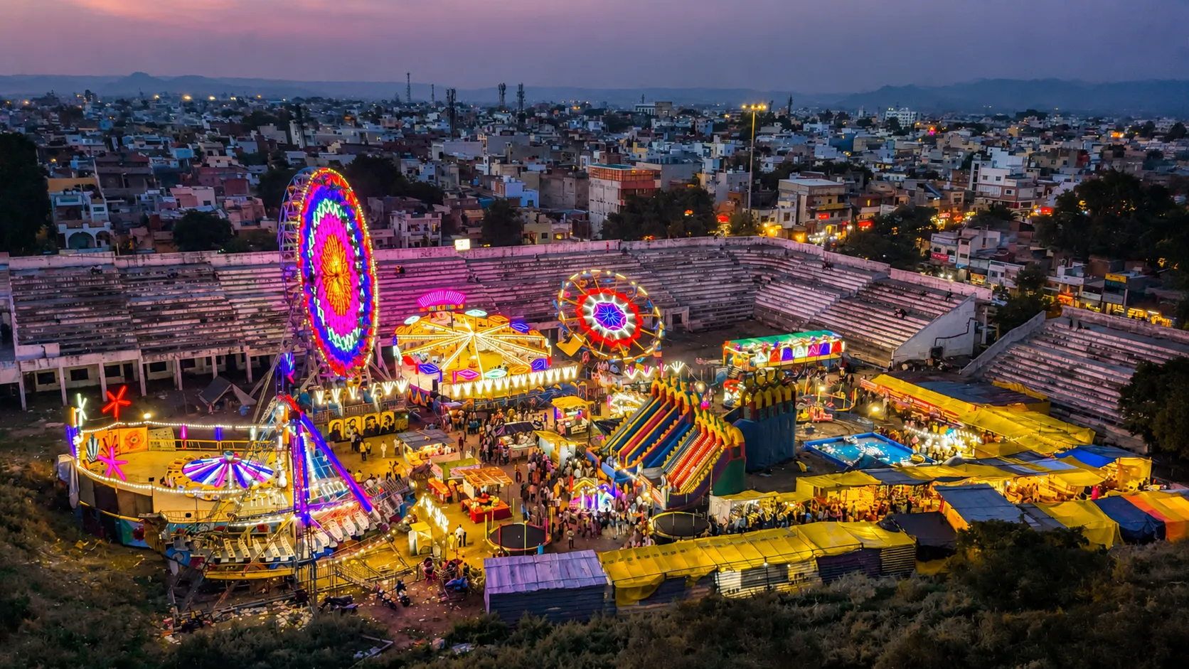 Colorful traditional fair with illuminated rides and stalls overlooking a city in Rajasthan at dusk