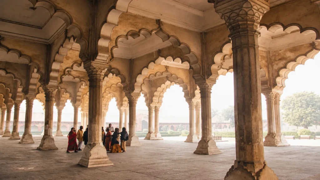 Historic Indian palace courtyard with ornate stone pillars, scalloped arches, and visitors exploring the hall.