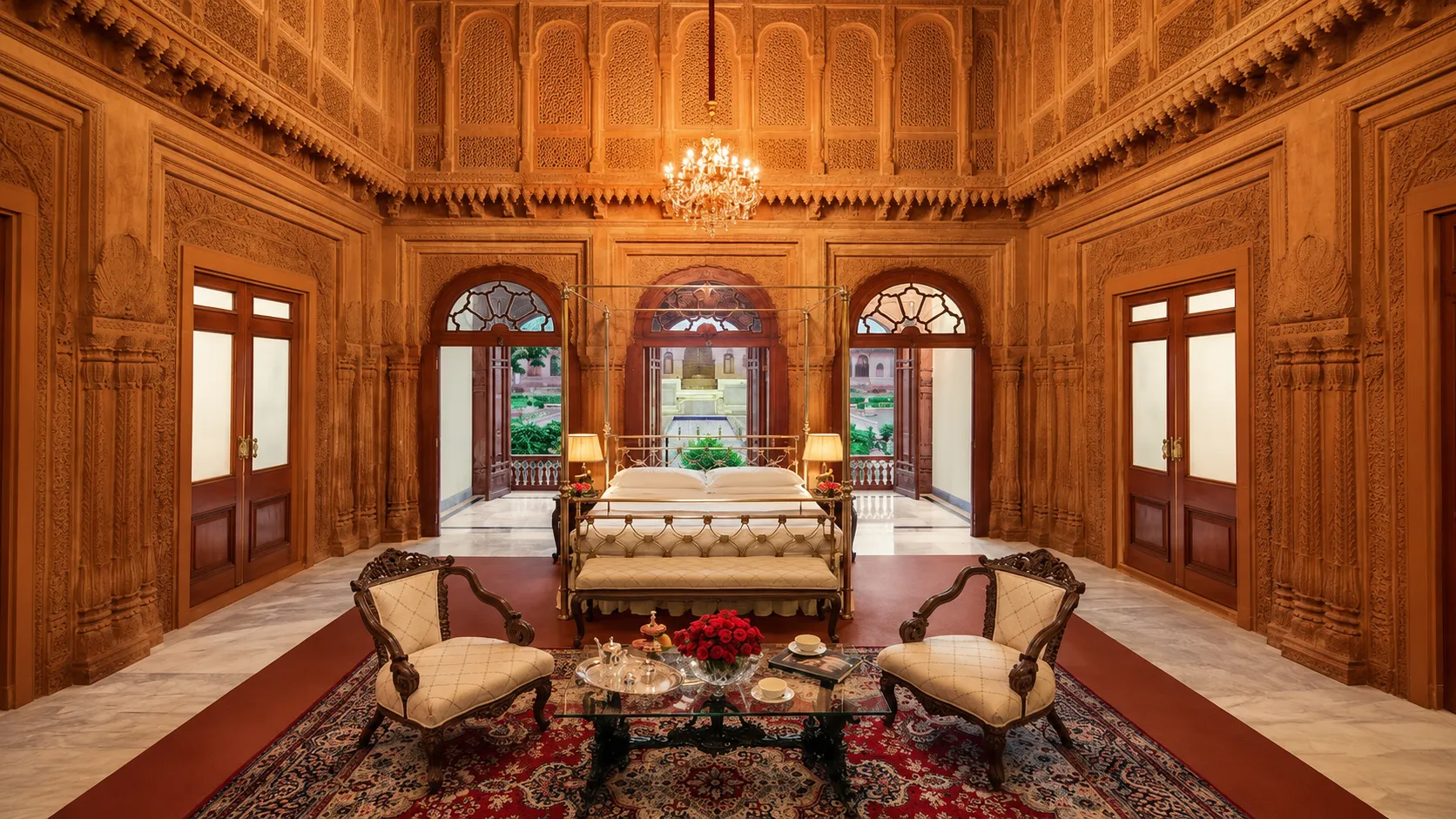 Luxury heritage suite featuring intricately carved wooden walls, a four-poster bed, chandelier, and elegant seating.