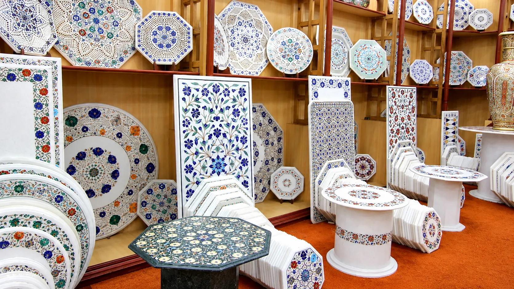 Showroom displaying white marble tables, decorative plates, panels, and stoneware featuring intricate colourful floral inlay designs