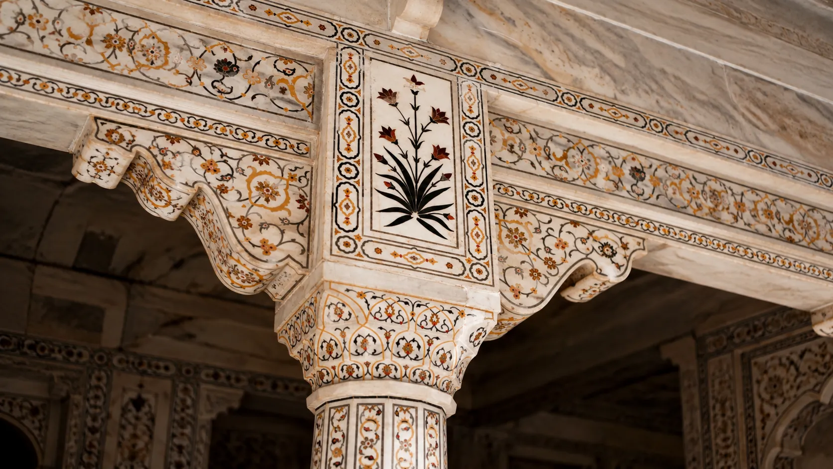 Ornate white marble column and arch decorated with floral pietra dura inlay and geometric patterns.