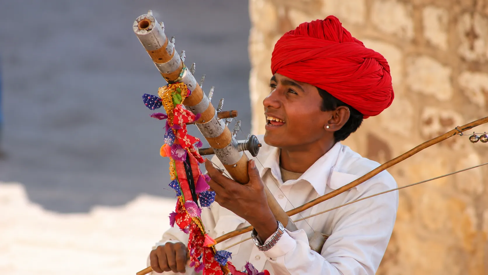 Rajasthani folk musician wearing a traditional red turban and playing a traditional musical instrument