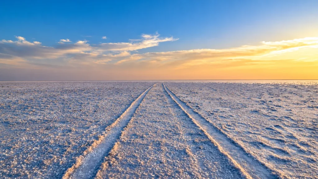 Tire tracks across the white salt desert of the Rann of Kutch beneath a blue and golden sunset sky