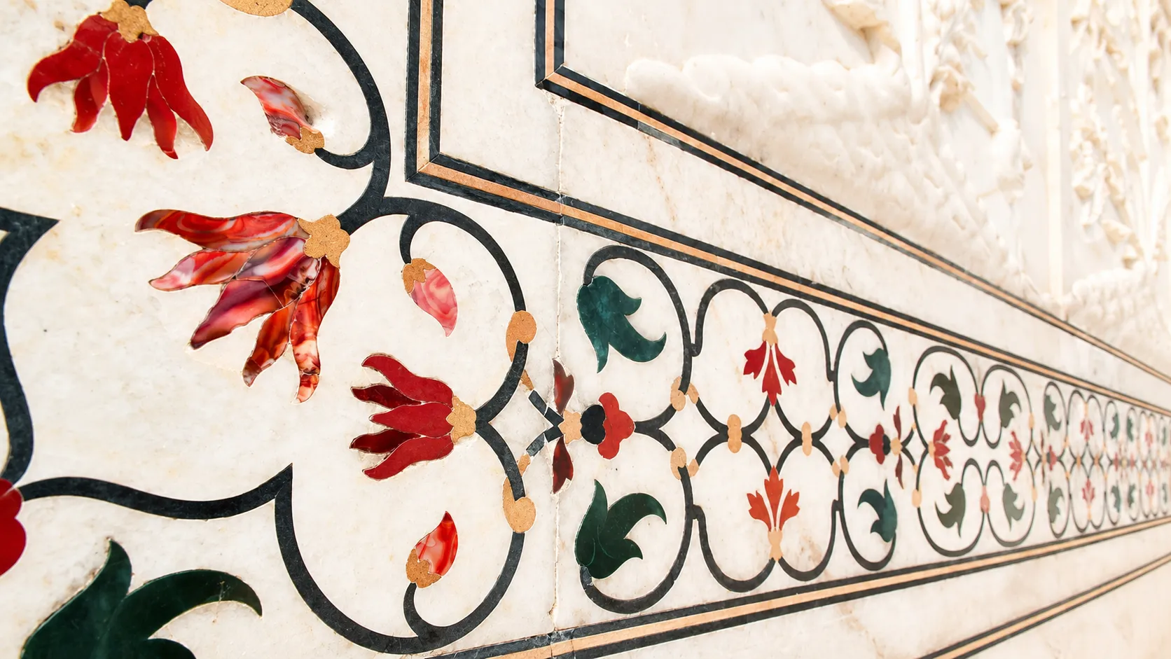 Close-up of an ivory marble border decorated with red and green floral stone inlay and dark ornamental scrollwork